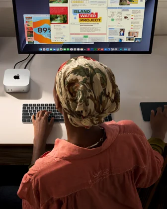 Una persona escribe en un escritorio que tiene una Mac mini, un monitor Studio Display conectado, un Magic Keyboard, un Magic Trackpad, varios artículos